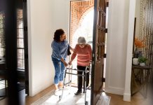The mid adult woman helps her senior adult friend carefully enter her home.