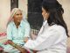 Female doctor examining indian senior adult woman with stethoscope during house visit in.