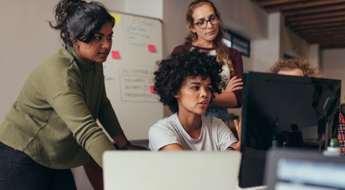 Software engineers working on project and programming in company. Startup business group working as team to find solution to problem. Woman programmer working on computer with colleagues standing by.