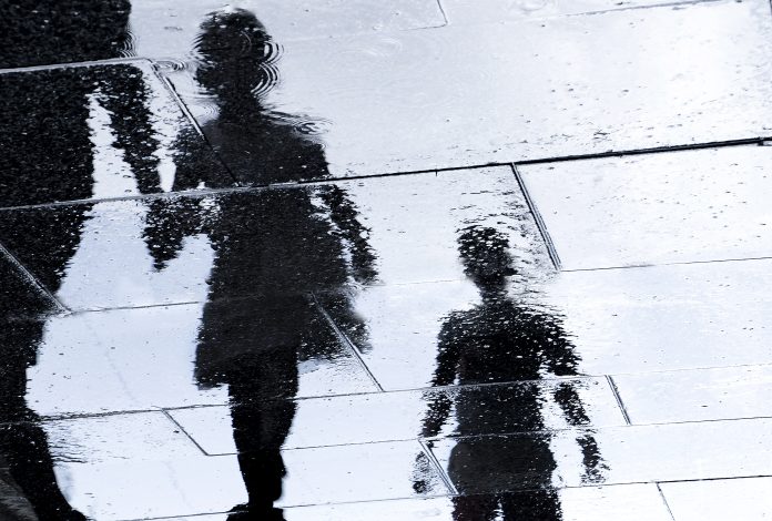 Blurry reflection shadow silhouette in a puddle of siblings and a parent walking wet city street