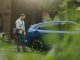 Portrait of a man charging his electric car in front of his house, plugging the charger into the charging port. The man is unplugging the charger from the fully charged car before going to the office.