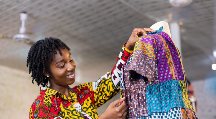 Smiling Ghanaian Dressmaker with locs hair measures a part of her colourful African pattern dress in her studio