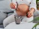 Beautiful young pregnant woman sitting on the sofa in the living room. Putting medicine drops in a glass of water. Close-up.