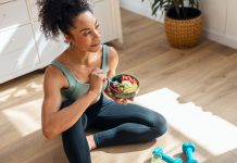 Athletic woman eating a healthy fruit bowl while sitting on floor in the kitchen at home