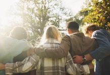 Group, back and friends to relax outdoor on school break, lens flare and hug for bonding in summer. People, students and embrace with support, care and trust together for social reunion at park
