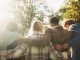 Group, back and friends to relax outdoor on school break, lens flare and hug for bonding in summer. People, students and embrace with support, care and trust together for social reunion at park