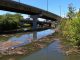 Garbage and debris pollute this waterway under an overpass.
