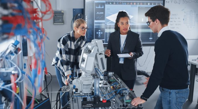 In Robotics Development Laboratory: Black Female Teacher and Two Students Work With Prototype of Robotic Hand. Young Student Telling Something with Smile and Brainstorming with Her Team.