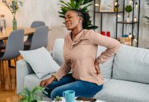 young black woman having back pain while sitting on the sofa at home.