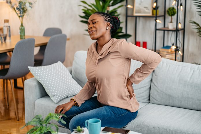 young black woman having back pain while sitting on the sofa at home.