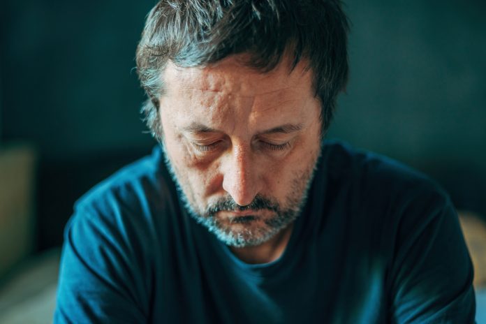 Unhappy contemplative mature adult man thinking in dark room, depressed sulking male pondering, selective focus