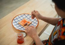 Woman Spreading Jam on Toast in a Bright Kitchen with Checked Plate and Jar of Jam, Close-Up of Hands and Food Preparation Process