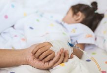 Mother hand holding sick daughter hand who have IV solution bandaged with love and care