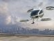 A generic white electric powered Vertical Take Off and Landing eVTOL aircraft with four rotors, coming in to land on roof top helipad with high city city buildings in the background. The sky is bright with clouds and it's late afternoon / early morning.