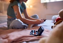 Close Up Of Diabetic Girl Sitting On Bed At Home Checking Insulin Levels On Mobile Phone App