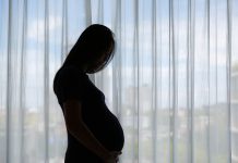 Silhouette of Pregnant Asian woman standing near window at home.