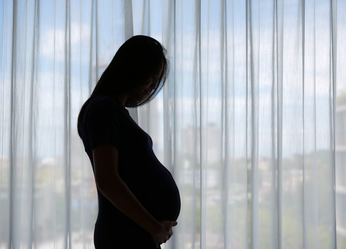 Silhouette of Pregnant Asian woman standing near window at home.