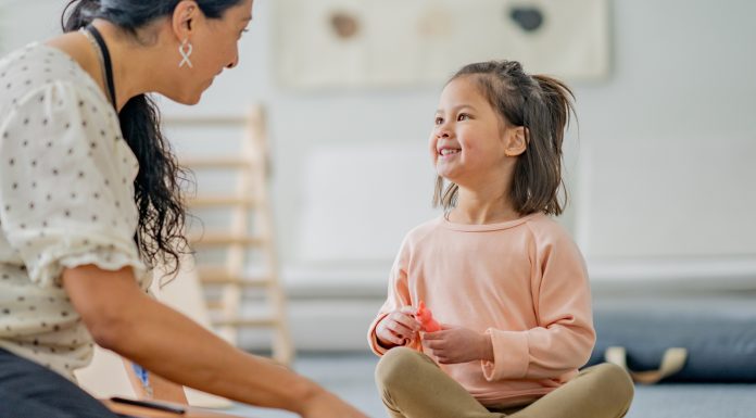 A Physiotherapist sits on the floor with a little girl during a therapy session. She is using toys and various colourful manipulatives to help aid the progress of the Therapy.