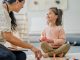 A Physiotherapist sits on the floor with a little girl during a therapy session. She is using toys and various colourful manipulatives to help aid the progress of the Therapy.