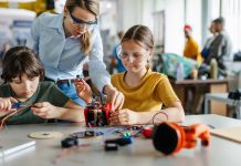 Female teacher helping to girls working on small robot, building robotic car in after-school robotics club. Children learning robotics in Elementary school. Girls in science.