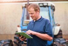 Production, farmer and man with tablet by tractor for schedule, checklist and research on industry. Farming, website and male person with tech for agriculture, agro app and reading weather info