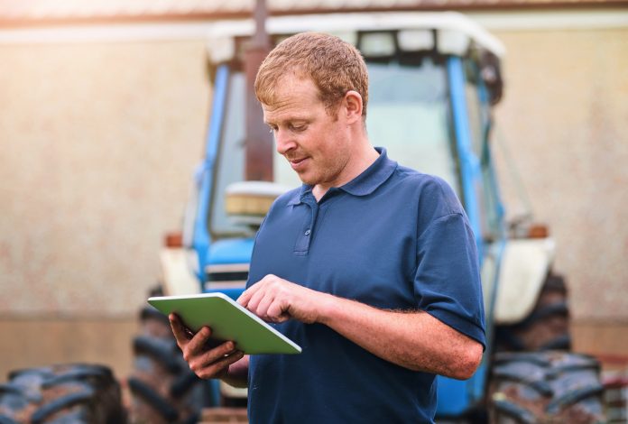 Production, farmer and man with tablet by tractor for schedule, checklist and research on industry. Farming, website and male person with tech for agriculture, agro app and reading weather info