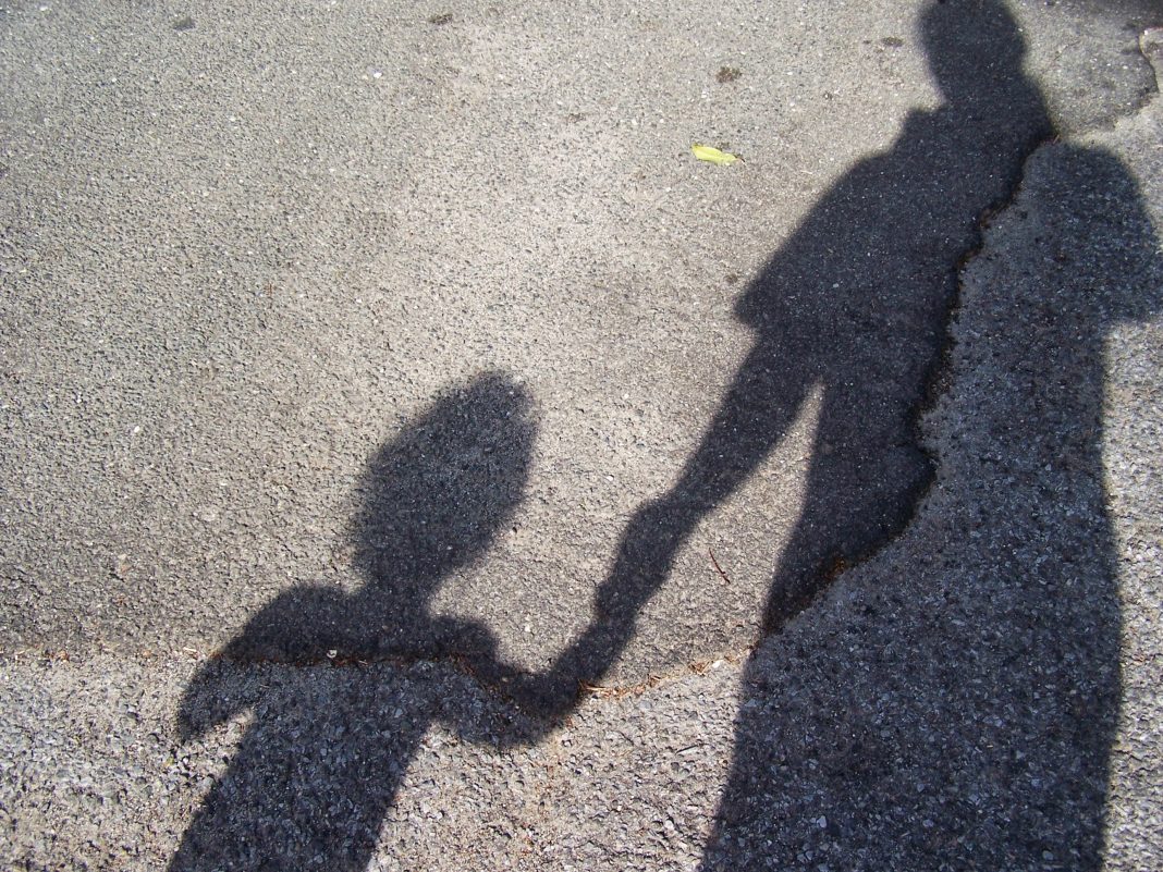 Shadow Of Mother With Son Standing On Road