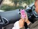 Over the shoulder view of a woman sitting in a van, using her mobile phone. She is smiling down at the screen in the North East of England. She is using a period tracking app, checking when her period is due.