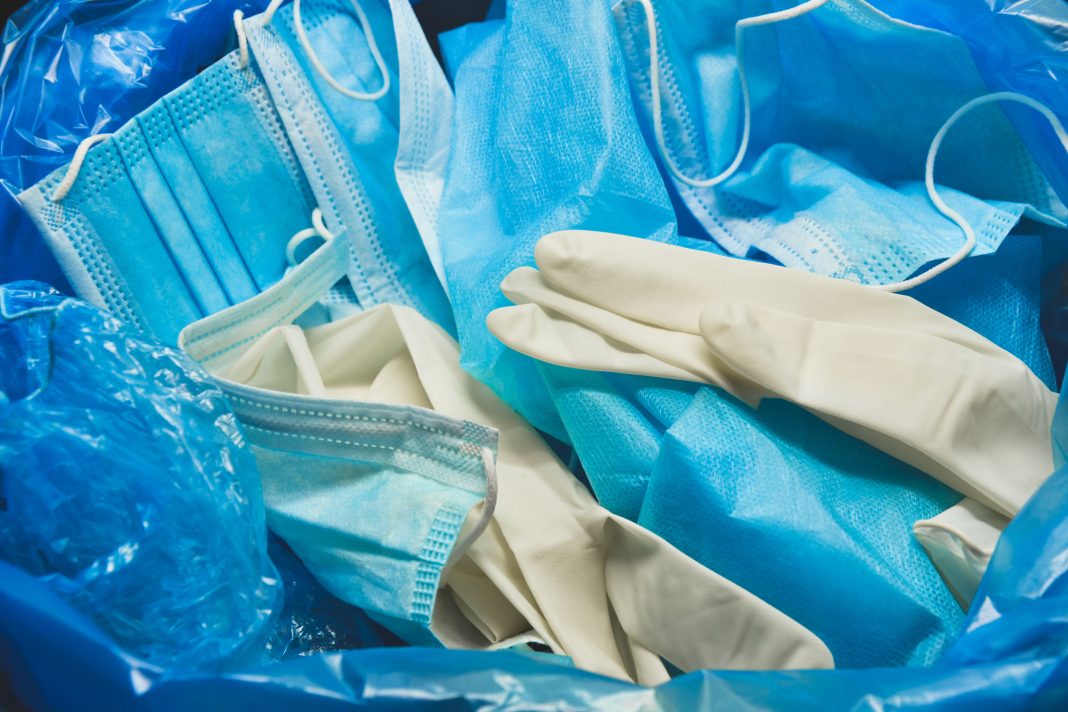 Medical trash. Coronavirus protection equipment in medical waste bin. Used face masks and sterile gloves. Doctor uniform for patient treatment in hospital. Prevention the spread of COVID-19.