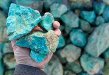 Blue green copper (Cu) oxide ore, held in hand, against background of ore that is out of focus. Mining.