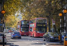 A two way street with busy traffic of driving cars and double double-decker buses in London in autumn