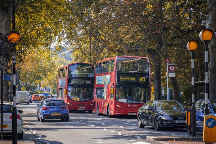 A two way street with busy traffic of driving cars and double double-decker buses in London in autumn