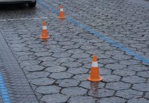Wet pavement in an urban parking lot features orange cones spaced evenly, indicating reserved spaces during a rainy day.