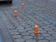 Wet pavement in an urban parking lot features orange cones spaced evenly, indicating reserved spaces during a rainy day.