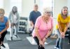 A small group of diverse seniors work out in a small fitness studio together. They are each dressed comfortably as they hold a stretch and focus on their breathing.