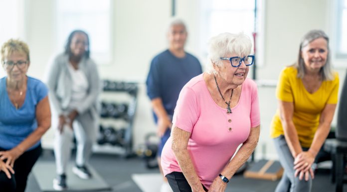A small group of diverse seniors work out in a small fitness studio together. They are each dressed comfortably as they hold a stretch and focus on their breathing.