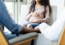 The unrecognizable stressed out parents in the foreground of the photo hold hands as they talk to their pregnant teen daughter.
