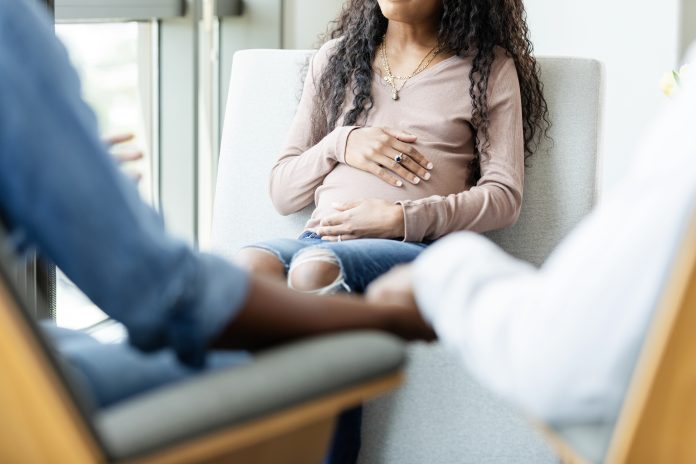 The unrecognizable stressed out parents in the foreground of the photo hold hands as they talk to their pregnant teen daughter.