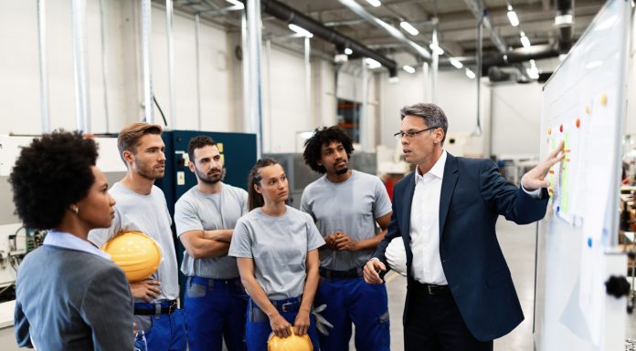 Corporate manager giving a presentation to group of factory workers and talking with them about future business development.