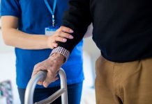 Senior Man With Hands On Walking Frame With Care Worker