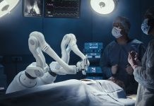 Two Surgeons Observing High-Precision Programmable Automated Robot Arms Operating Patient In High-Tech Hospital. Robotic Limbs Performing Complicated Nanosurgery, Doctors Looking At Vitals On Monitor.