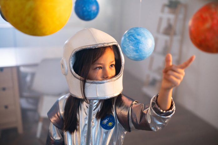 Girl in a space suit playing at home, exploring and learning about planets, imagining space travel.