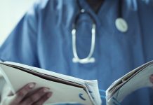 A doctor with a Stethoscope around his neck looking at a patients file.