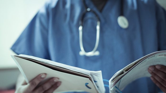 A doctor with a Stethoscope around his neck looking at a patients file.