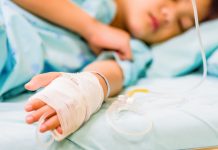 Closeup kid hand sleeps on a bed in hospital with saline intravenous.