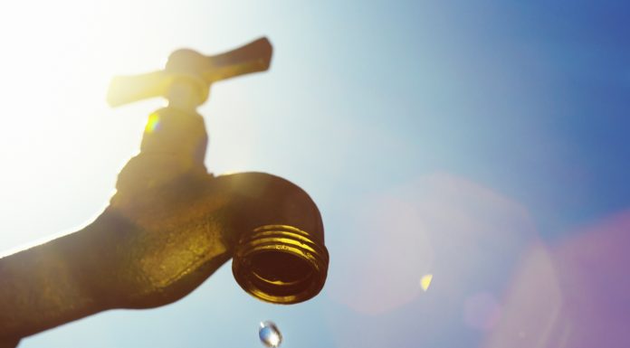 A single droplet falls from a faucet, symbolizing water scarcity or drought.