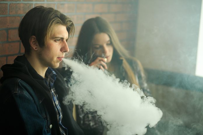 Vape teenagers. Young cute girl in sunglasses and young handsome guy smoke an electronic cigarettes in the vape bar. Bad habit that is harmful to health. Vape teenagers. Young cute girl in sunglasses and young handsome guy smoke an electronic cigarettes in the vape bar. Bad habit that is harmful to health. Vaping activity.