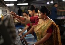 Indian female coworkers dressed in saris operating equipment producing spools in textile factory and representing women empowerment