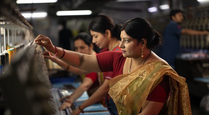Indian female coworkers dressed in saris operating equipment producing spools in textile factory and representing women empowerment