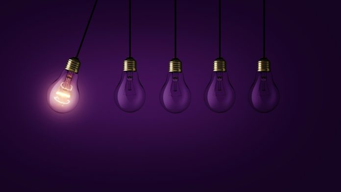 Creative light bulb lights up other extinguished light bulbs on a dark purple background, concept. Leadership, creative idea. Think differently. Start up